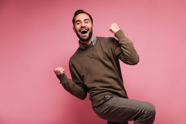 Happy man celebrates victory and smiles on pink background .